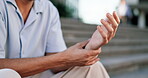 Hand, wrist pain and arthritis with a man outdoor, sitting on steps and feeling his joint for stiffness. Medical, anatomy and osteoporosis with a male suffering from an injury or broken bone