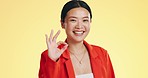 Smile, ok sign and face of Asian woman on yellow background for perfect, good job and agreement. Emoji mockup, hand gesture and portrait of happy girl in studio with success, okay symbol and yes icon