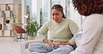 Stomach cramps, woman and doctor consultation with a patient in pain from constipation. Office, abdomen and colon problem of a young female with a healthcare, wellness and clinic worker on a couch