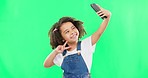 Phone, selfie and child peace sign in a studio with happiness from profile picture. Isolated, green background and young girl with technology showing a v hand gesture for social media with a smile