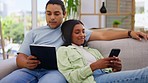 Couple, tablet and phone scroll together on a living room sofa with love looking at social media. Web search, happy woman and man on a lounge couch at home watching online videos and texting in house