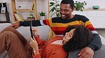 Black couple, tablet and relax on couch in home living room with comic smile, chat and social media video. Man, woman and touch screen for lying, love bond and funny meme on web, app ux and internet
