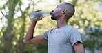 Fitness, drinking water and man in a park for exercise, training or morning cardio. Thirsty, hydration and athletic guy relax with drink in forest after running, walking or wellness routine in nature