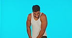 Portrait, playful and a shy man on a blue background in studio feeling funny with humor while joking. Funny, comedy and goofy with a silly young hispanic man playing coy in a tank top or vest