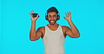 Headphones, dancing and man face isolated on blue background for fitness music, winning and celebration on phone. Dance, workout or celebrate energy of indian person listening to audio tech in studio