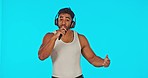 Singer, rapper or man with headphones and microphone in studio to sing or rap on blue background. Male model, artist or musician dancing for hip hop music performance for a live convert or event