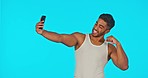 Phone, selfie and man in studio with peace, thumbs up and positive expression on blue background. Personal trainer, bodybuilder or social media health influencer pose for blog, web or profile picture
