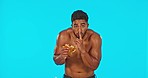 Hiding, burger and face of a man on cheat day isolated on a blue background in a studio. Sneaky, looking and portrait of a fitness guy eating an unhealthy meal while on a health journey with mockup