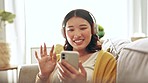 Video call, wave and phone of a woman on a living room sofa with communication and happiness. Headphones, Asian female and gen z person on a mobile and web conversation at home on a lounge couch