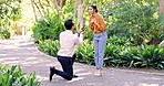 Propose, engagement and question with a man asking a woman, will you marry me, in a garden during summer. Love, romance and ring in a box with a young couple bonding on a date in a park together