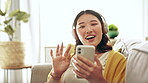 Video call, hand wave and phone of a woman on a living room sofa with communication and happiness. Headphones, Asian female and gen z person on a mobile and web conversation at home on a lounge couch