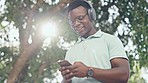 Music, smartphone and black man with headphones in park, walking in trees with sun and happy smile. Streaming, wifi and happiness, young person listening to audio on phone with online radio service.