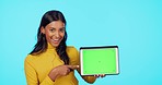 Happy woman, tablet and pointing to mockup on green screen with tracking markers against a blue studio background. Portrait of female showing touchscreen display for product placement or advertising