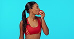 Health, apple and thumbs up with woman in studio for fitness, diet and nutrition. Happy, approval and wellness with female eating fruit isolated on blue background for self love, workout and detox