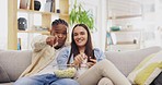 Couple, popcorn and watching tv in home, pointing and bonding on sofa in living room. Face portrait, interracial and happy black man and woman streaming television, movie or film while eating food.