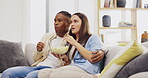 Couple, eating popcorn and watching tv in home, bonding and relax on sofa in living room. Television, interracial and black man and woman streaming movie, video or film while chewing food or snack.