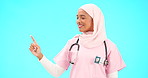 Face, nurse and Muslim woman pointing to mockup in studio isolated on a blue background. Portrait, healthcare professional and happy Islamic person with marketing, advertising or product placement.