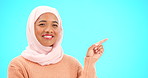 Muslim woman, happy and portrait pointing finger at space for mockup, advertising or promotion. Islam female with hand, smile and hijab for product placement announcement or sale on blue background