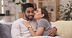 Happy, love and couple relaxing on a sofa talking, bonding and spending quality time together. Happiness, conversation and young woman kissing boyfriend on the cheek while sitting in the living room.