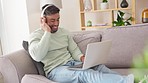 Laptop, headphones and man on a sofa in the living room listening to music, playlist or album. Happy, dance and male streaming a song, radio or audio while browsing on internet with computer at home.