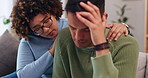 Couple is sad, woman comforting man with empathy, support and love while sitting in living room at home. Grief, loss and mental health with depression, stress and people in relationship in crisis