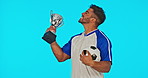 Win, football and face of a man with a trophy isolated on a blue background in studio. Happy, success and portrait of a soccer player kissing an award for winning a game, achievement and celebrating