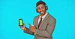 Headphones, phone and business man with green screen in studio isolated on blue background mockup. Face portrait, pointing and happy Indian person streaming music with marketing or product placement.