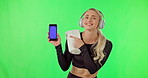 Woman, dancing and phone with music on green screen with headphones, smile and website or app. Happy athlete person dance for fitness workout and listening to audio and pointing at smartphone
