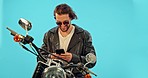 Phone, motorbike and happy man in studio on blue background for road trip, texting and leather aesthetic. Smartphone, motorcycle and man on internet for gps, location and online maps search isolated 