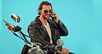 Phone call, man and motorbike in studio on blue background for road trip, freedom and fun with biker aesthetic. Smartphone, conversation and guy driver with motorcycle for vacation, journey or riding