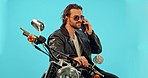 Phone call, motorbike and man in studio on blue background for road trip, freedom and fun with biker aesthetic. Smartphone, conversation and guy driver with motorcycle for vacation, journey or riding