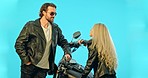 Talking, motorcycle and couple on blue background in conversation, flirting and speaking in studio. Love, dating and happy man and woman chatting on motorbike for road trip, adventure and travel