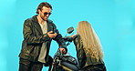 Talking, motorcycle and couple conversation in studio or love, phone and speaking together on blue background. Woman, man and happy with motorbike leather jacket on road trip, journey or discussion 