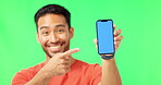 Asian man, phone and pointing to mockup on green screen with tracking markers against a studio background. Portrait of happy male showing smartphone display for advertising or marketing on copy space