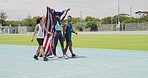 Team of patriotic athletes celebrating victory, walking and cheering on a track outside. Three diverse american runners carrying the US national flag after winning silver and gold medals.