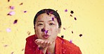 Studio, asian woman blowing confetti and celebration for birthday, anniversary or celebrating Chinese new year. Happy party, smile and model from china on yellow background to celebrate with glitter