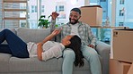 Happy couple, keys and relax on sofa in new home with game, playing and bonding with love for goal. Man, woman and happiness for young homeowner, achievement and comic with boxes, package or property