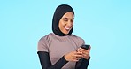 Phone, happy and muslim woman in a studio networking on social media, mobile app or the internet. Happiness, smile and islamic female model browsing online with cellphone isolated by blue background.