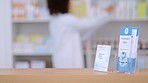 Focus on an information pamphlet on a counter at a pharmacy, advertising treatment and health care with a pharmacist packing rows medication on a shelf in a modern drugstore against blur background