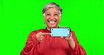 Phone, pointing and portrait of a woman on green screen for announcement, advertising or website. Happy mature person with smartphone and tracking markers for marketing, internet or network promotion