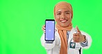 Muslim woman, doctor and thumbs up with phone mockup on green screen against a studio background. Portrait of female medical or healthcare expert with like emoji, smartphone app and tracking markers