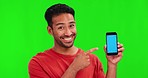 Man, face and point at cellphone by green screen with smile, review and choice with mock up space for app logo. Student guy, phone and happy for decision for branding, agreement and studio portrait