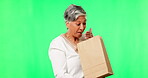 Shopping, wow and a senior woman on a green screen background in studio looking surprised or excited by a package. Retail, silly and a mature customer holding a gift, present or bag in anticipation