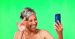 Senior woman, phone and video call in green screen studio with wave, smile or excited in mockup by background. Mature lady, webinar and smartphone for communication, social network or happy for hello