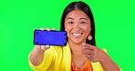 Woman face, green screen and hand pointing to phone mockup with tracking markers on studio background. Portrait, space and asian lady person showing product placement for news or how to steps for app