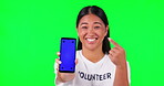 Green screen, phone and volunteer woman pointing at charity website, fund information or mockup. Asian person laugh for smartphone sign up or register for nonprofit, NGO or donation tracking markers