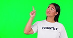 Volunteer, green screen and woman pointing finger at space for advertising, charity or information. Happy asian person with tshirt and looking up for nonprofit project, NGO help or donation in studio