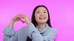 Woman, heart hand and portrait with a smile and love emoji sign in a studio. Asian female person, happy and valentines day icon gesture with pink background and hope for romance and kindness