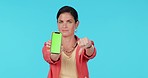 Woman, thumbs down and show phone with green screen, mock up space and bad review for app by blue background. Businesswoman, angry or upset with blank smartphone, emoji or sign language for feedback