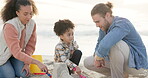 Family, child and sand castle at beach together for holiday, vacation or bonding fun. Man and woman parents play with interracial girl and bucket toys for quality time, travel adventure and wellness